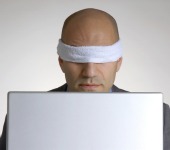 Blindfolded man on computer. Image courtesy of Shutterstock